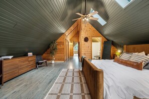 Une chambre aménagée en mezzanine avec un plafond en pente, un lit, un bureau et une chaise.