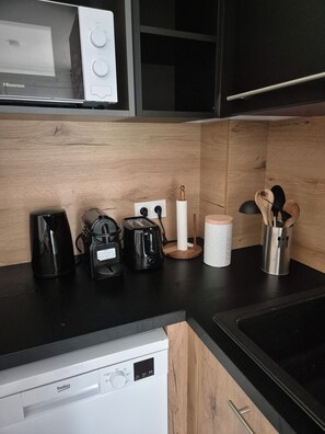 A kitchen with a black countertop, a coffee maker, a toaster, a microwave, and a dishwasher. - Charming T2 in Lecci - Terrace, air conditioning and 3 swimming pools 2 steps from the beaches (Lecci)