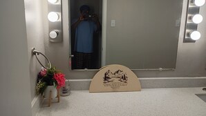 Une salle de bain avec un miroir, des luminaires, un porte-serviettes, une petite plante et un panneau décoratif.