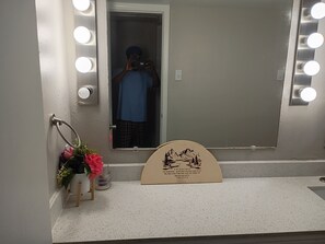 A bathroom with a mirror, lights, a towel ring, a small plant, and a decorative sign. - Apartment providing one bedroom and bathroom. In Richardson with AC and comfort (Richardson)
