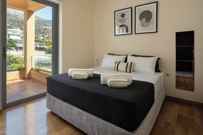 A modern hotel room with a large bed, a view of the outdoors, and two framed abstract artworks on the wall. - Modern Sea View Apartment with Balcony on the Athenian Riviera (Anavissos)