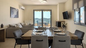 Zona pranzo con tavolo in legno apparecchiato per quattro persone, divano, televisione e balcone con vista.