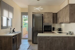A modern kitchen with wooden cabinets, a stainless steel refrigerator, and a unique ceiling light fixture. - Modern Sea View Apartment with Balcony on the Athenian Riviera (Anavissos)