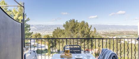 A balcony with a table set for two, a chair, and a view of distant mountains.