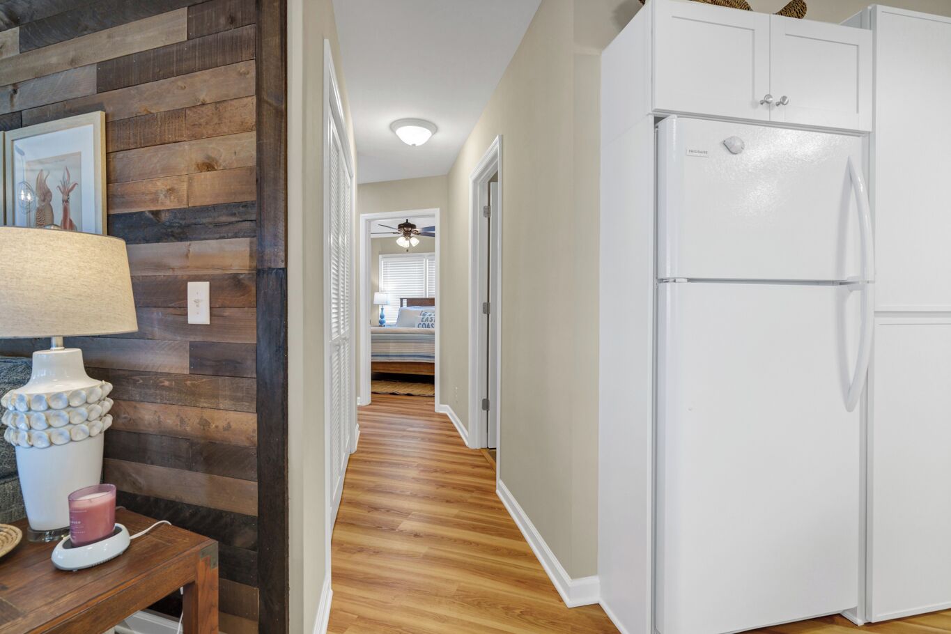 A kitchen with a white refrigerator, wooden flooring, and a dining area with a table and lamp.