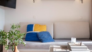 Ein modernes Wohnzimmer mit einer Couch, einem Couchtisch, einer Pflanze und einem an der Wand befestigten Flachbildfernseher.