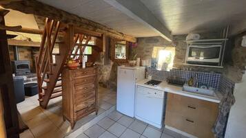 Una cocina compacta con un mueble de madera, un refrigerador blanco, un horno empotrado y una pared de piedra.