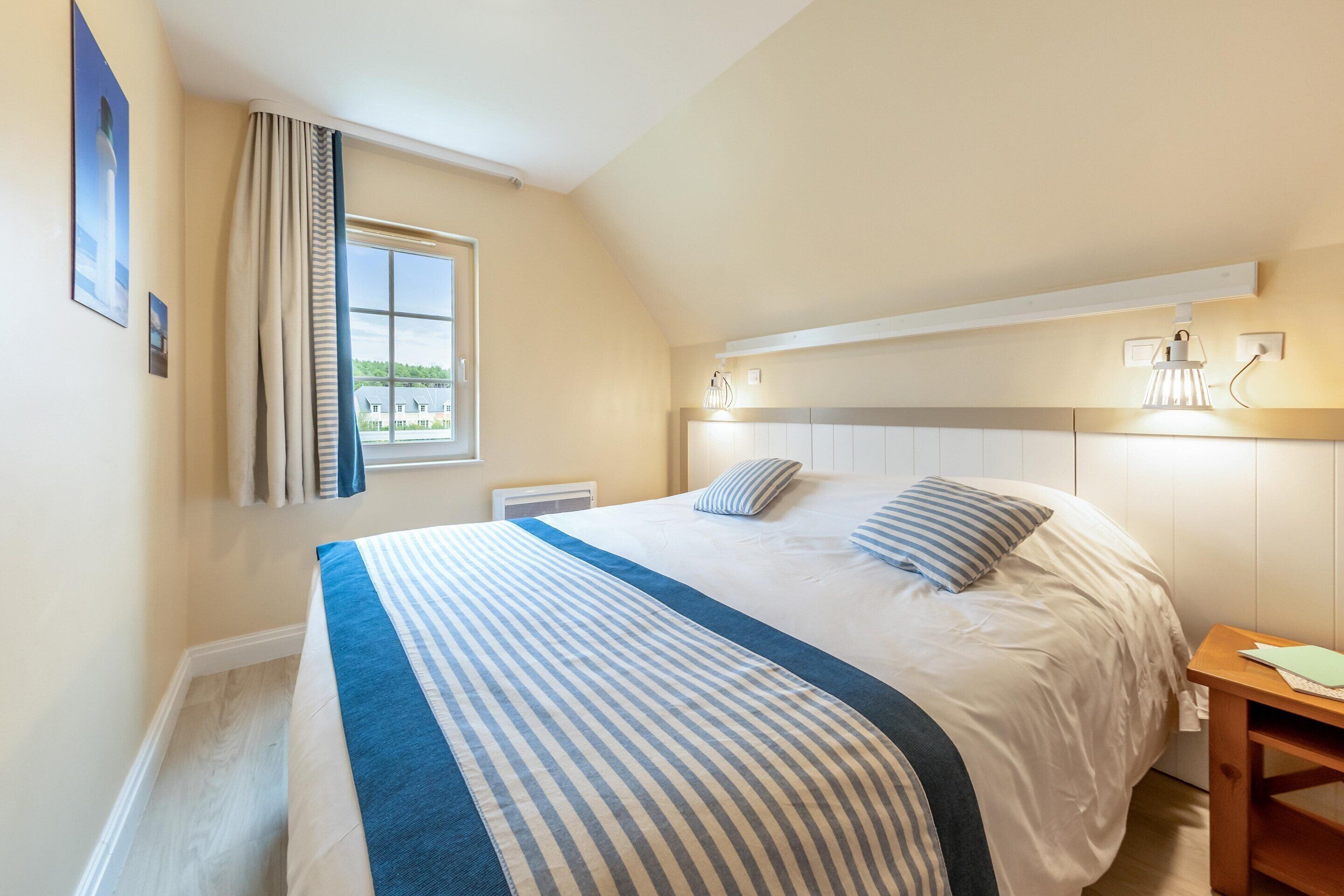 A bedroom with a bed, a window, a nightstand, and a wall-mounted light fixture.