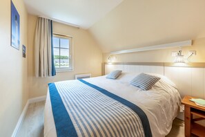 Une chambre à coucher comprenant un lit, une fenêtre, une table de chevet et un luminaire fixé au mur.
