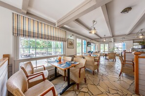 Un restaurant avec de hauts plafonds, de grandes fenêtres, des chaises en osier et un sol en pierre.
