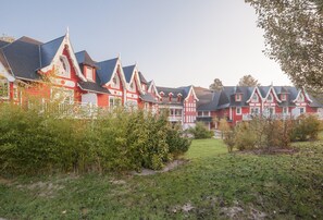 Une rangée de maisons traditionnelles aux toits pentus, peintes en rouge et en blanc, avec des boiseries blanches, le tout entouré de verdure.