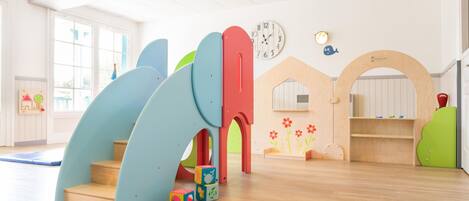 A children's play area with a slide, play structures, and a clock on the wall.