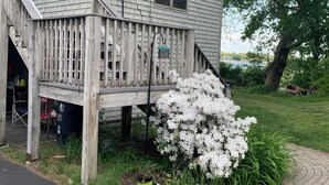 A two-story house with a wooden deck, a small porch, and a large white flowering bush. - Spacious, sunlit, seaside 4-bedroom, 3 bath waterfront house w/ AC in Warren, RI (Warren)