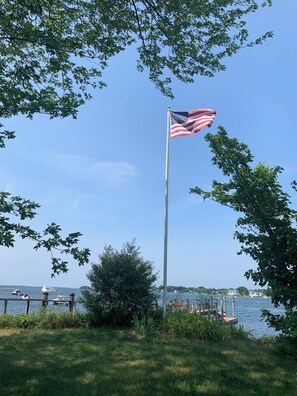 A flagpole with an American flag, a grassy area, and a body of water with boats. - Spacious, sunlit, seaside 4-bedroom, 3 bath waterfront house w/ AC in Warren, RI (Warren)