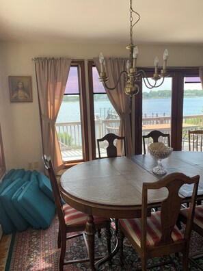 A dining area with a table, chairs, a chandelier, and a view of a body of water through large windows. - Spacious, sunlit, seaside 4-bedroom, 3 bath waterfront house w/ AC in Warren, RI (Warren)