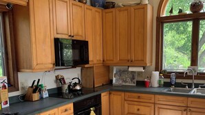 A kitchen with wooden cabinets, a microwave, a stove, and a window with a view of trees. - Spacious, sunlit, seaside 4-bedroom, 3 bath waterfront house w/ AC in Warren, RI (Warren)