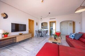 A modern living room with a flat-screen TV, a red sofa, a dining table with chairs, and a kitchen area visible through an open door. - Mediterranean & golf dreams (Mutxamel)