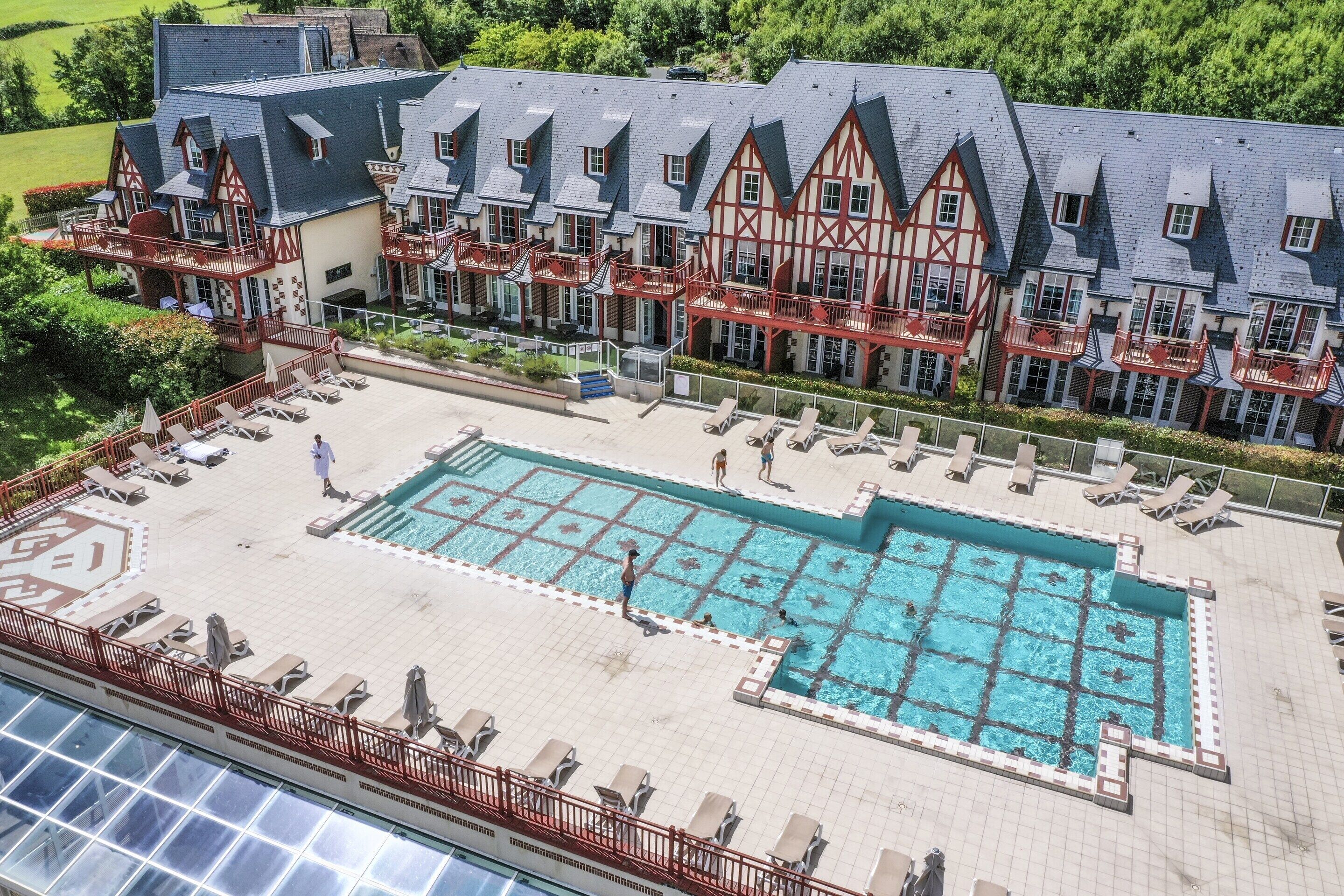 A hotel with a large swimming pool, multiple balconies, and a traditional European architectural style.