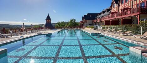 A swimming pool with a tiled pattern, lounge chairs, and a building with a balcony.