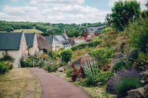 A pathway leading to traditional houses with steep roofs, surrounded by lush greenery and flowering plants. - Houlgate Duplex for 8 With Spa (Houlgate)
