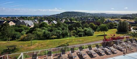 Terraza en la azotea con sillones de sol, piscina y vistas a un barrio residencial.