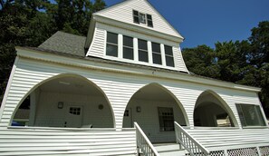 Un edificio bianco con tetto a triangolo, diverse finestre e un portico ad archi.