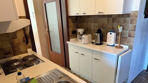 A kitchen with a stainless steel sink, a stove, white cabinets, and a coffee maker.