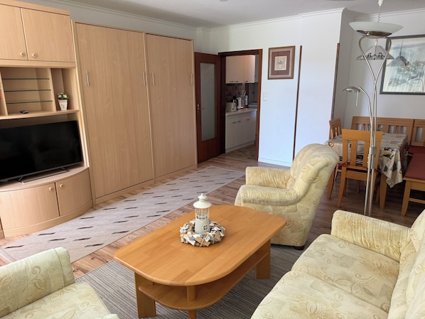 A living room with a TV, sofa, armchair, wooden cabinets, and a dining area with a table and chairs.
