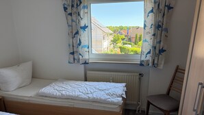 A bedroom with two beds, a window with curtains, a radiator, and a chair.
