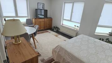 Ein Schlafzimmer mit einem Bett, einem Schreibtisch mit Lampe, einem Sessel, einem Fernseher und einem Deckenventilator.