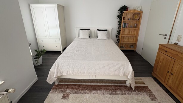 A bedroom with a bed, two bedside tables, a wardrobe, a wooden cabinet, and a potted plant. - Cozy bright 1 room apartment in Bramsche max. 3 persons (Bramsche)