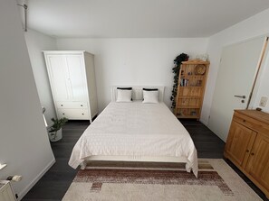 Ein Schlafzimmer mit einem Bett, zwei Nachttischen, einem Kleiderschrank, einem Holzschrank und einer Topfpflanze.