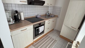 A modern kitchen with light wood cabinets, a black range hood, a built-in oven, a coffee maker, and a sink. - Cozy bright 1 room apartment in Bramsche max. 3 persons (Bramsche)