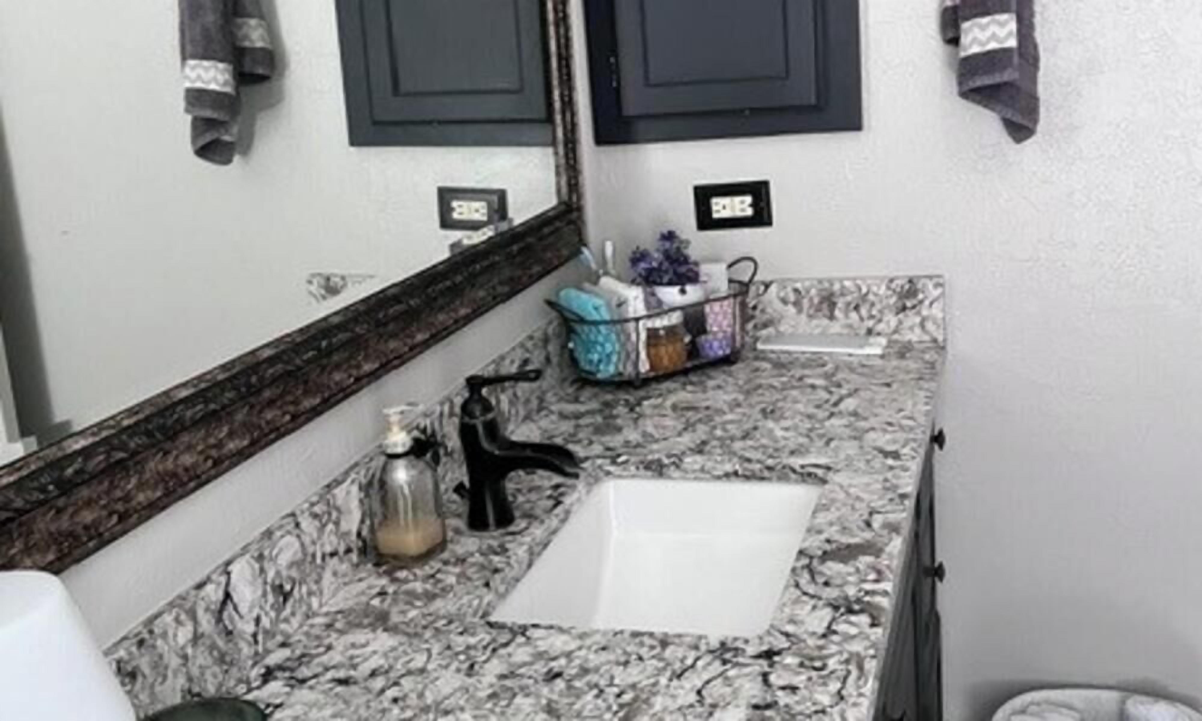 A bathroom with a marble countertop, a sink, a mirror, and a towel rack.