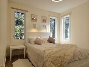 A bedroom with a bed, bedside table, and two windows.
