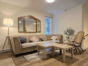 A living room with a sofa, a coffee table, a floor lamp, a rocking chair, and a mirror.