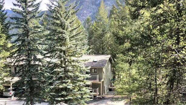 A lodge surrounded by evergreen trees, with a mountain in the background. - Home away from Home in the Heart of Nature (East Kootenay G)