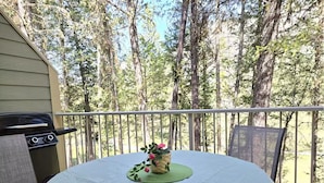 A round table with a green placemat and a floral centerpiece on a balcony with a railing, overlooking a forested area. - Home away from Home in the Heart of Nature (East Kootenay G)