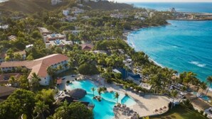 Vogelperspektive eines Resorts mit großem Schwimmbad, Strandhäusern und üppiger Vegetation.