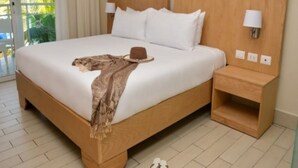 Ein Hotelzimmer mit einem großen Bett, einem Nachttisch, einer Lampe, einem Hut und Hausschuhen auf dem Boden.