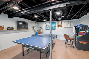 Ein Tischtennis-Tisch mit Ballmaschine, einem Fernseher und einem Poster an der Wand.