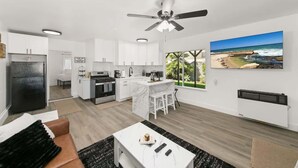 A modern kitchen with white cabinets, a black refrigerator, and a dining area with a white table and chairs. - 1 Bedroom Steps from Beach and Carlsbad Village (Carlsbad)