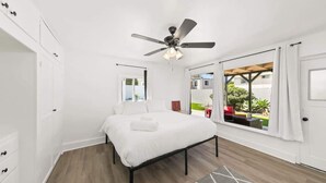A bedroom with a bed, a ceiling fan, a window with curtains, and a view of the outside. - 1 Bedroom Steps from Beach and Carlsbad Village (Carlsbad)