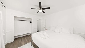 Una habitación blanca con cama, ventilador de techo y vestidor.