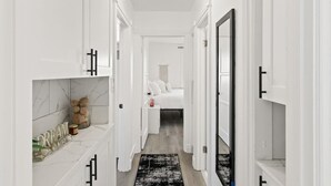 Un pasillo estrecho con paredes y puertas blancas, un tapete negro y una cama a lo lejos.