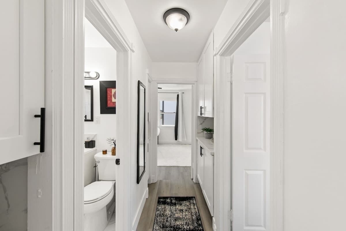 Un couloir étroit avec des toilettes, des tableaux encadrés et une porte donnant sur une salle de bain.