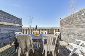A wooden deck with a table and chairs, a wooden fence, and a view of mountains. - Family Duplex Stay for 6 in Ardeche (Grospierres)