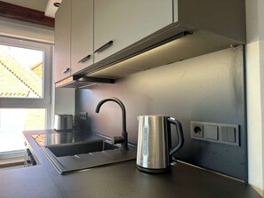 Una cucina moderna con un bollitore in acciaio inossidabile, un lavandino e una finestra che si affaccia su un edificio in mattoni.
