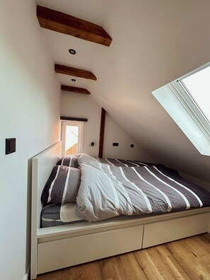 A loft-style bedroom with a sloped ceiling, a skylight, a bed with striped bedding, and exposed wooden beams. - Stylish ANTJE Apartment in STRAND HAUS 10 (Borkum)