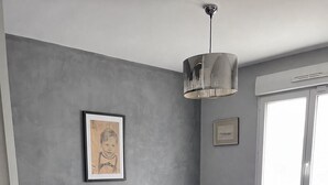 Ein Schlafzimmer mit einem Bett, einem Nachttisch, einem gerahmten Bild, einer Pendelleuchte und einem Fenster.
